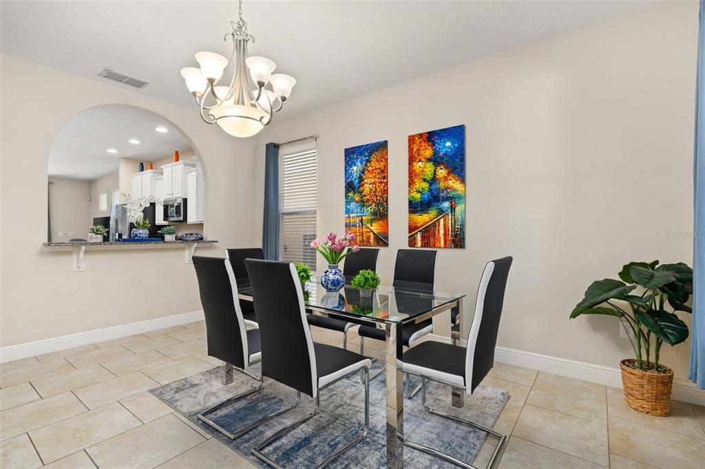 A dining room features a glass table, six black chairs, a chandelier, and two wall paintings — 5373 OAKBOURNE AVENUE, DAVENPORT, FL