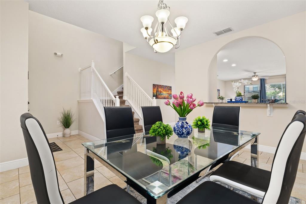 A dining room features a glass-topped table, black chairs, and a staircase in the background — 5373 OAKBOURNE AVENUE, DAVENPORT, FL