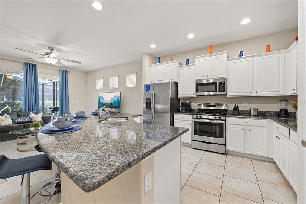 A kitchen features white cabinets, granite countertops, stainless steel appliances, and an island with seating — 5373 OAKBOURNE AVENUE, DAVENPORT, FL