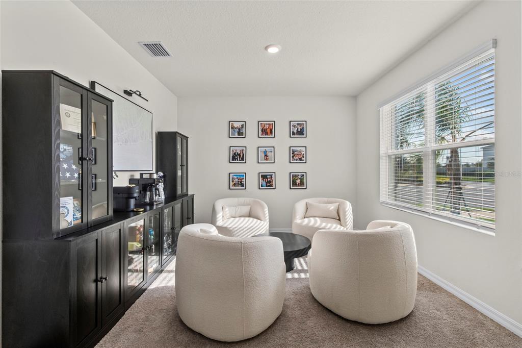 A home office features four white armchairs, a black storage cabinet, and a grid of photos — 8210 DOLPHIN BLUFF BOULEVARD, WESLEY CHAPEL, FL