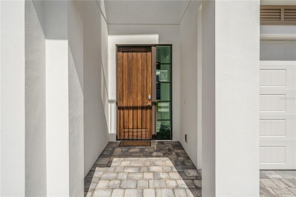 A wooden front door with a glass sidelight sits under a covered entryway with pavers — 119 OCEAN ESTATES DRIVE, HUTCHINSON ISLAND, FL
