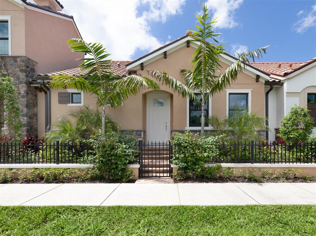 The exterior of a tan stucco house features a gated front entrance and palm trees — 930 E VENICE AVENUE, VENICE, FL