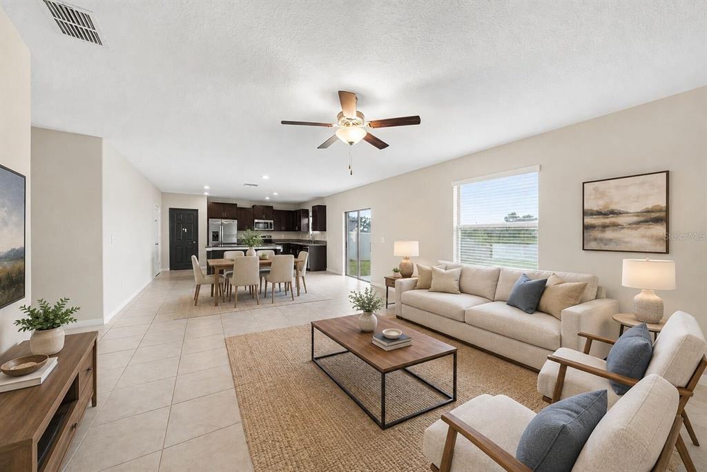 An open-concept living room and kitchen with tile flooring, neutral walls, and modern furnishings — 1507 GOLDEN GLOW DRIVE, RUSKIN, FL