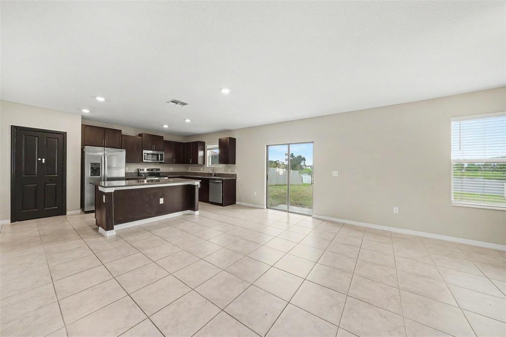 An open-concept kitchen and living area features dark wood cabinets, tile flooring, and sliding doors — 1507 GOLDEN GLOW DRIVE, RUSKIN, FL
