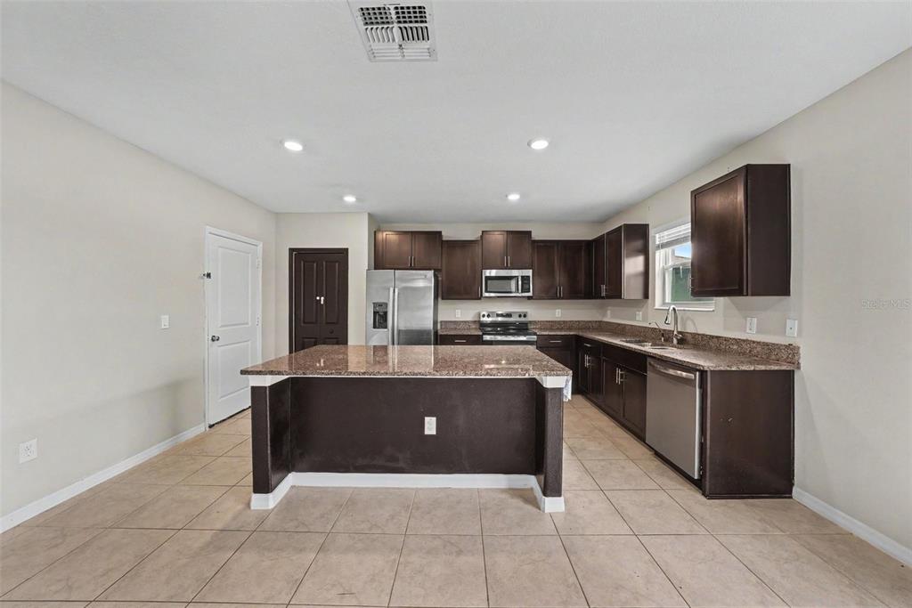A kitchen features dark wood cabinets, granite countertops, a center island, and stainless steel appliances — 1507 GOLDEN GLOW DRIVE, RUSKIN, FL