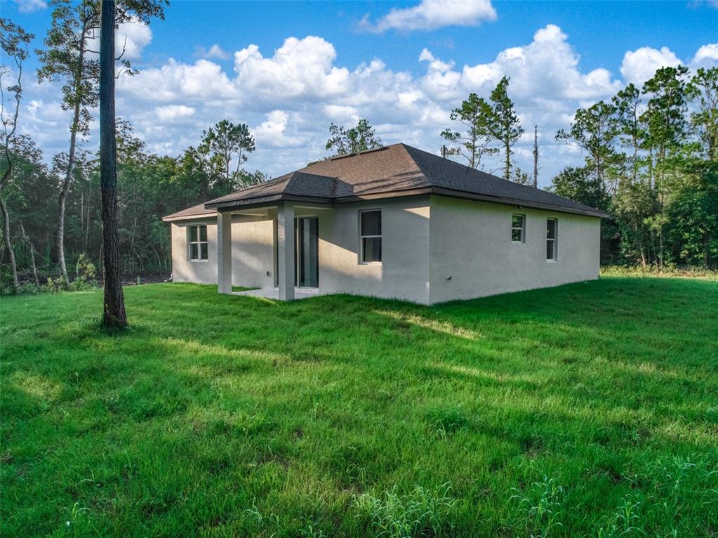 The rear exterior of a single-story stucco house features a covered patio and wooded surroundings — 8636 SUN N LAKE BOULEVARD, SEBRING, FL