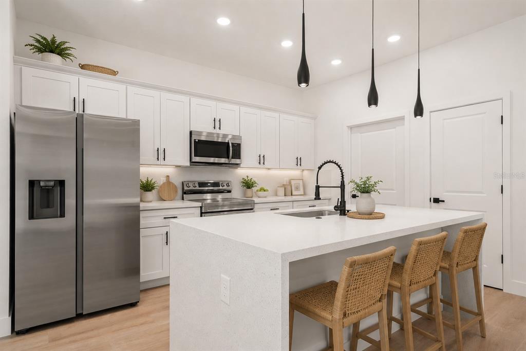 A modern kitchen features white cabinetry, stainless steel appliances, a quartz island, and three pendant lights — 8636 SUN N LAKE BOULEVARD, SEBRING, FL