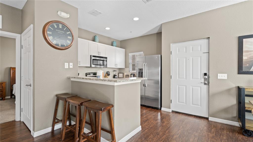 A kitchen features a breakfast bar with three stools, white cabinets, and stainless steel appliances — 5350 DIPLOMAT COURT UNIT 104, KISSIMMEE, FL