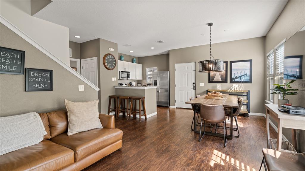 An open-concept living and dining area features a leather sofa, kitchen island, and wood flooring — 5350 DIPLOMAT COURT UNIT 104, KISSIMMEE, FL