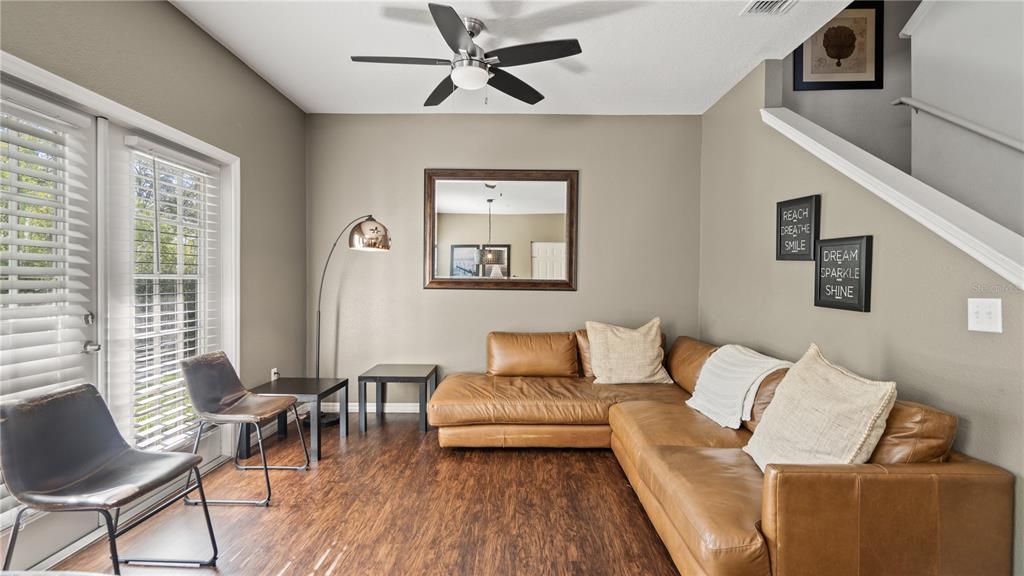 A living room features a brown leather sectional, wood-look flooring, a ceiling fan, and wall art — 5350 DIPLOMAT COURT UNIT 104, KISSIMMEE, FL