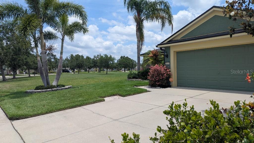 A view of a house exterior with a green garage door, driveway, and palm trees — 9820 50TH STREET CIRCLE E, PARRISH, FL