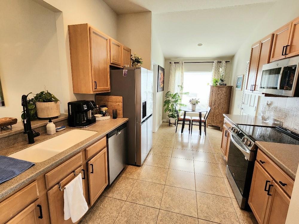 A kitchen with light wood cabinets, stainless steel appliances, and a dining area at the end — 9820 50TH STREET CIRCLE E, PARRISH, FL
