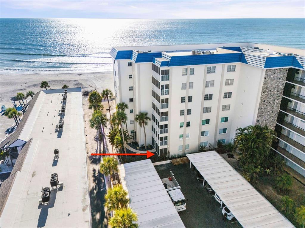 An aerial view shows a multi-story beachfront condominium building with covered parking and palm trees — 800 BENJAMIN FRANKLIN DRIVE UNIT 110, SARASOTA, FL