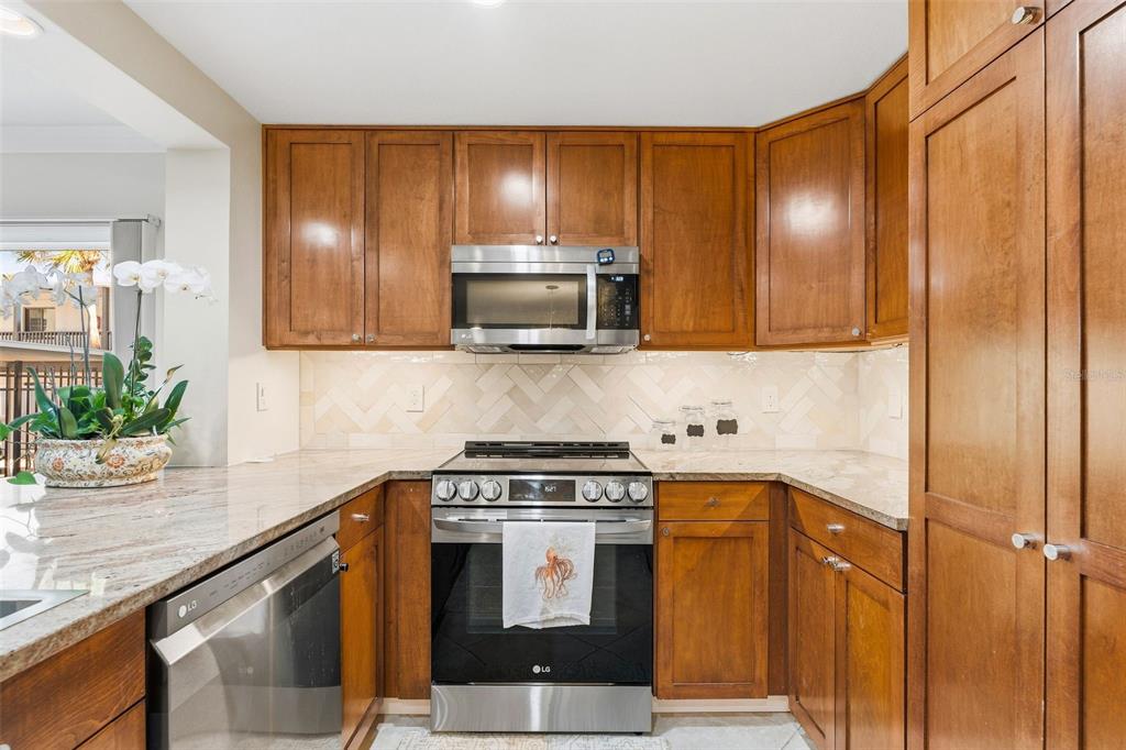A kitchen features wood cabinets, stainless steel appliances, granite countertops, and a herringbone tile backsplash — 800 BENJAMIN FRANKLIN DRIVE UNIT 110, SARASOTA, FL