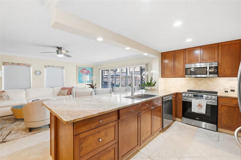 A kitchen with wood cabinets and granite countertops opens into a living room area — 800 BENJAMIN FRANKLIN DRIVE UNIT 110, SARASOTA, FL