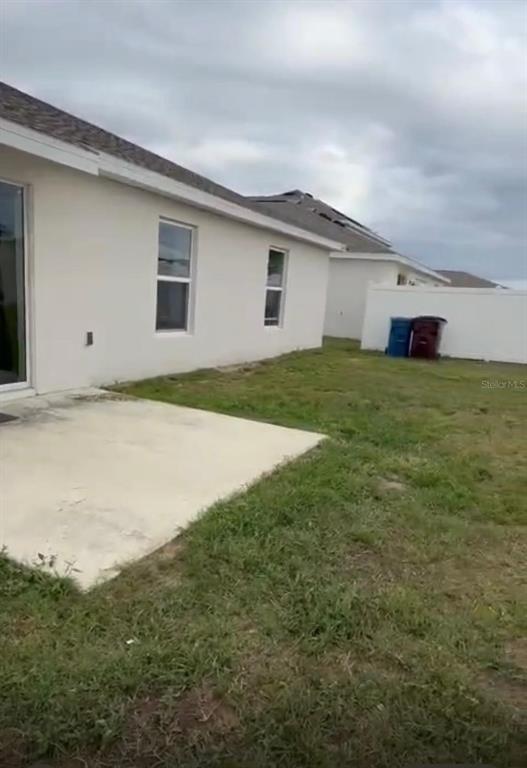 A concrete patio sits outside the back of a white house with a fenced yard — 1946 POND PINE COURT, HAINES CITY, FL