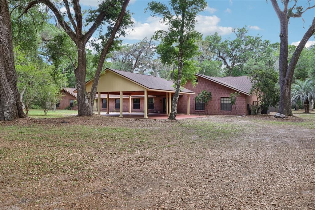 A single-story brick house with a large covered patio sits on a wooded lot — 2685 CR 564, BUSHNELL, FL