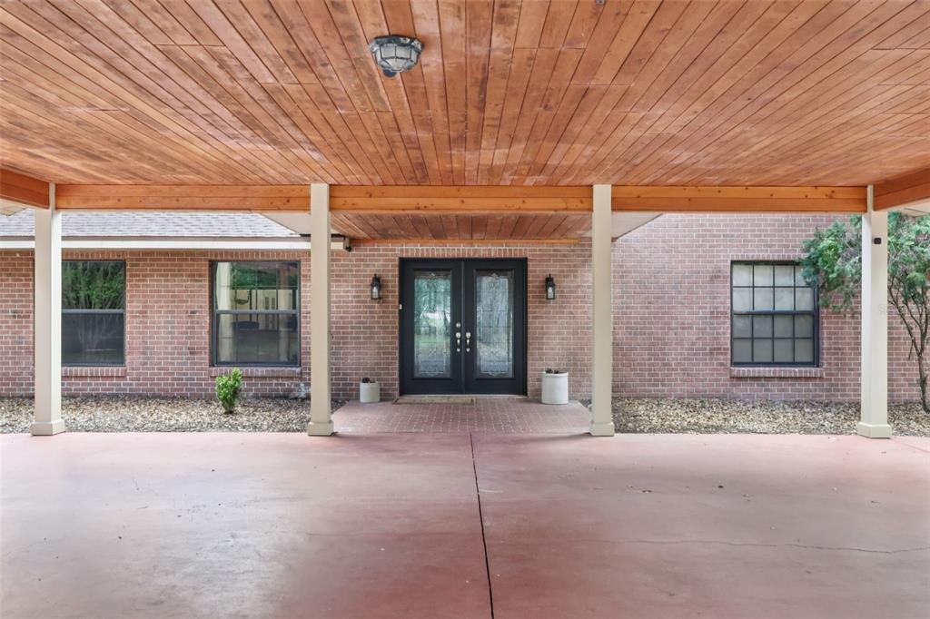 A covered brick patio features a wood-paneled ceiling, support columns, and double glass entry doors — 2685 CR 564, BUSHNELL, FL