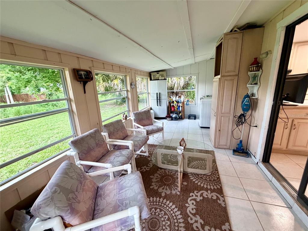 A sunroom features tile flooring, a patterned area rug, white furniture, and large windows — 3010 YULE TREE DRIVE, EDGEWATER, FL