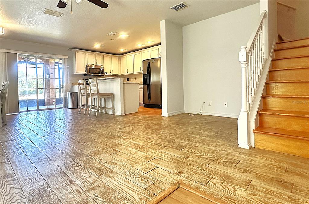 An open-concept kitchen and living area features wood-look tile flooring and a wooden staircase — 2048 SUN DOWN DRIVE, CLEARWATER, FL