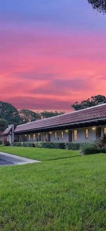 A long, single-story building with a tiled roof sits behind a grassy lawn at sunset — 1701 PINEHURST ROAD UNIT 16G, DUNEDIN, FL