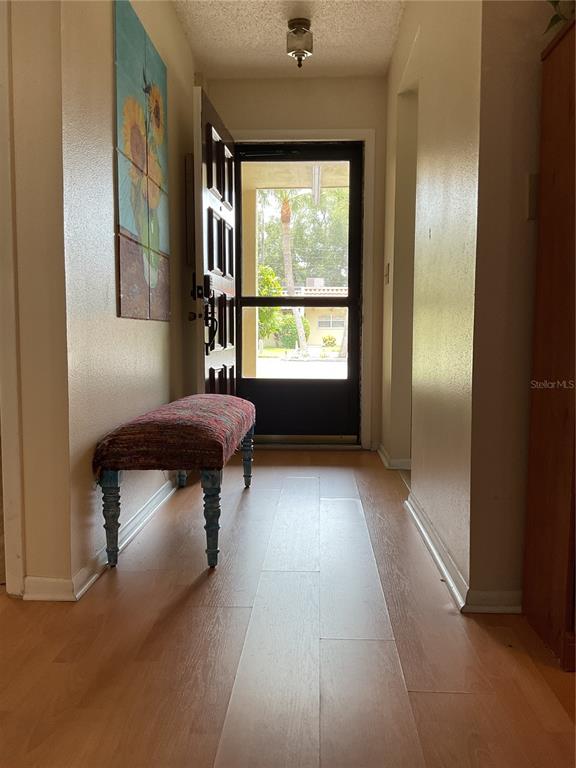 An entryway features light wood-look flooring, a patterned bench, and a door with a screen — 1701 PINEHURST ROAD UNIT 16G, DUNEDIN, FL