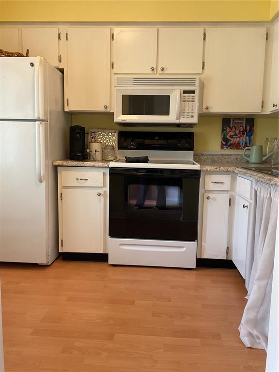 A kitchen features white cabinetry, a black stove, a white microwave, and light wood flooring — 1701 PINEHURST ROAD UNIT 16G, DUNEDIN, FL