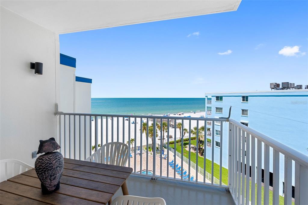 A balcony with a wooden table and an owl statue overlooks the beach and ocean — 18450 GULF BOULEVARD UNIT 508, INDIAN SHORES, FL