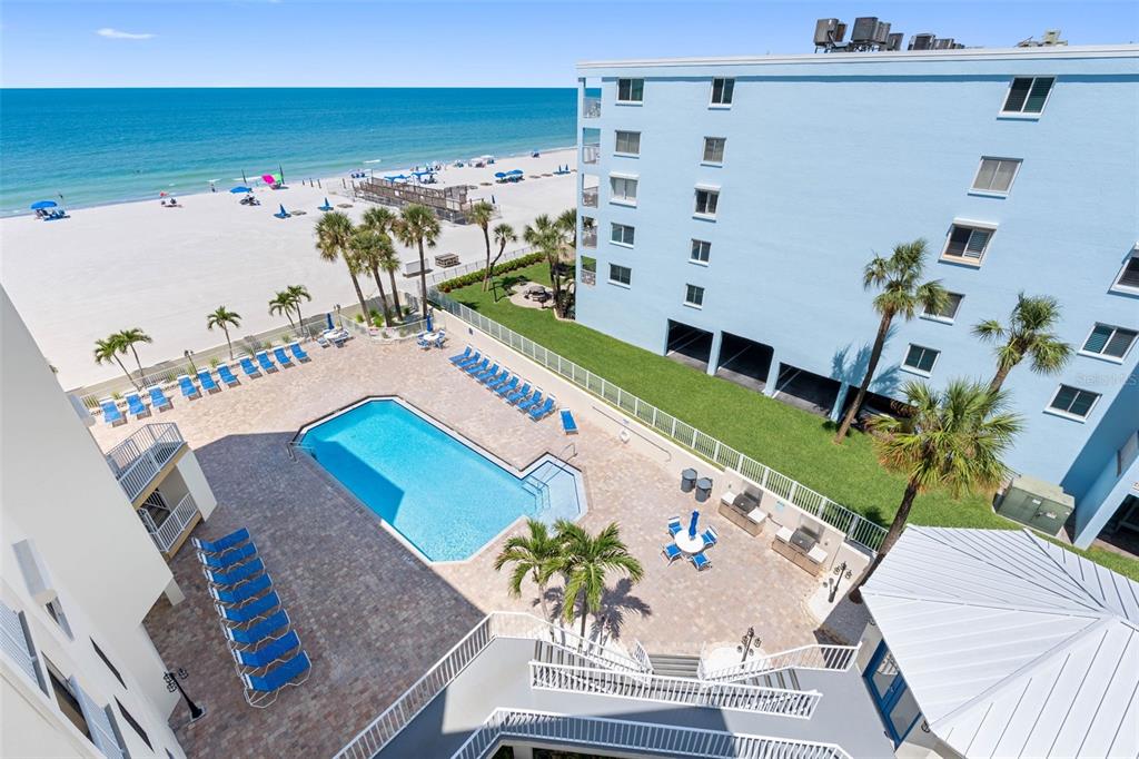 An elevated view of a swimming pool, patio, and beach area next to a blue building — 18450 GULF BOULEVARD UNIT 508, INDIAN SHORES, FL
