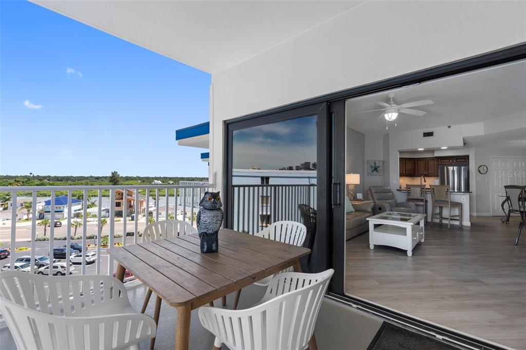 A balcony with a wooden table and chairs overlooks a parking lot and water — 18450 GULF BOULEVARD UNIT 508, INDIAN SHORES, FL