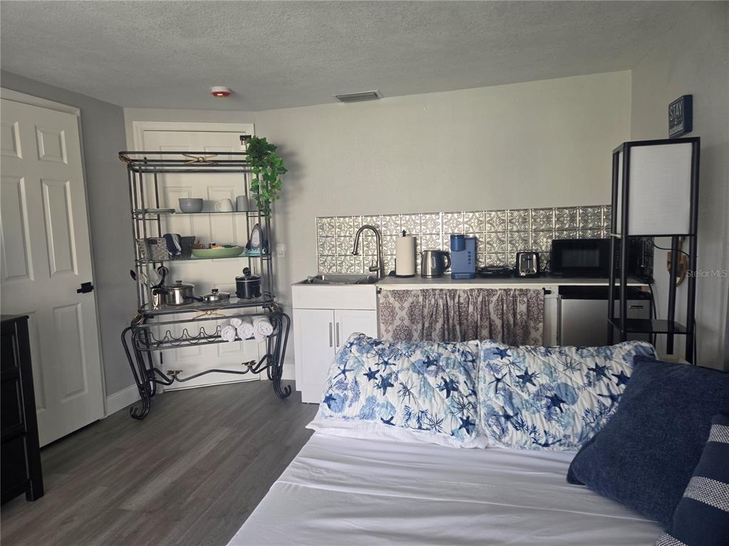 A bedroom features a kitchenette with a sink, patterned backsplash, and a metal storage rack — 12700 5TH ISLE, HUDSON, FL