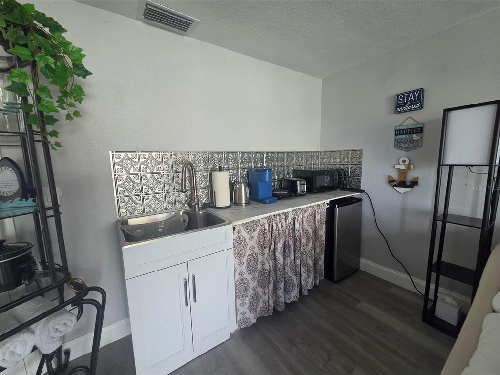 A kitchenette features a stainless steel sink, patterned backsplash, white cabinet, and a curtained base — 12700 5TH ISLE, HUDSON, FL