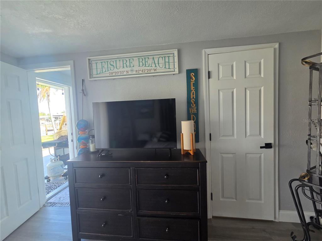 A bedroom features a dark wood dresser, a television, and a door leading outside — 12700 5TH ISLE, HUDSON, FL