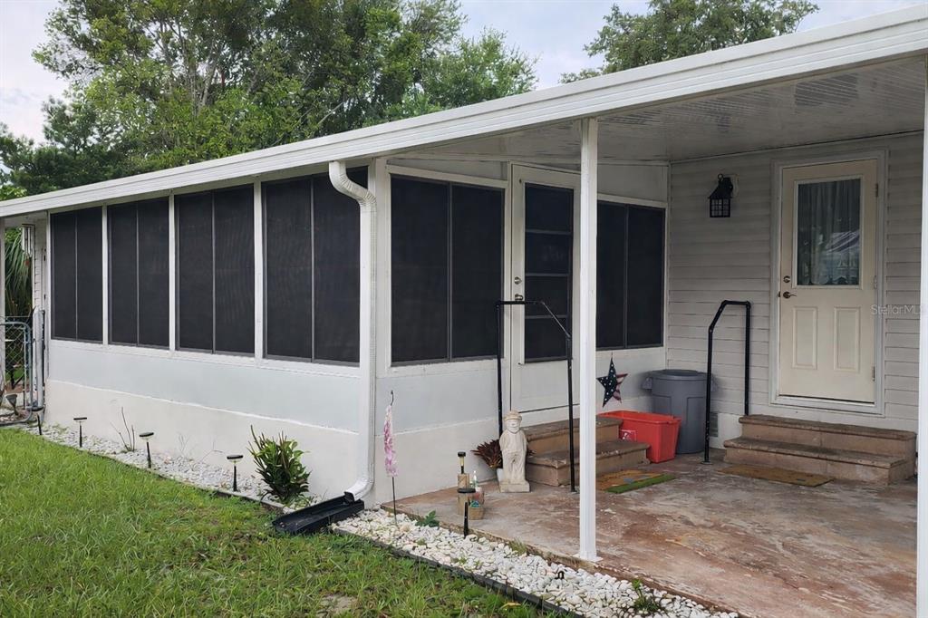 A mobile home exterior features a screened-in porch, a concrete patio, and white siding — 121 PINE TREE DRIVE, DEBARY, FL