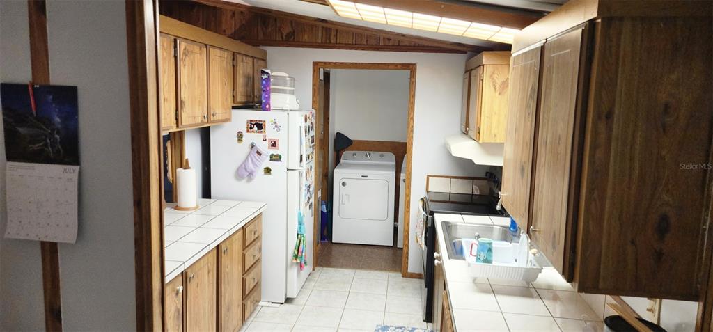 A kitchen with wood cabinets, white tile countertops, and a doorway leading to a laundry area — 121 PINE TREE DRIVE, DEBARY, FL