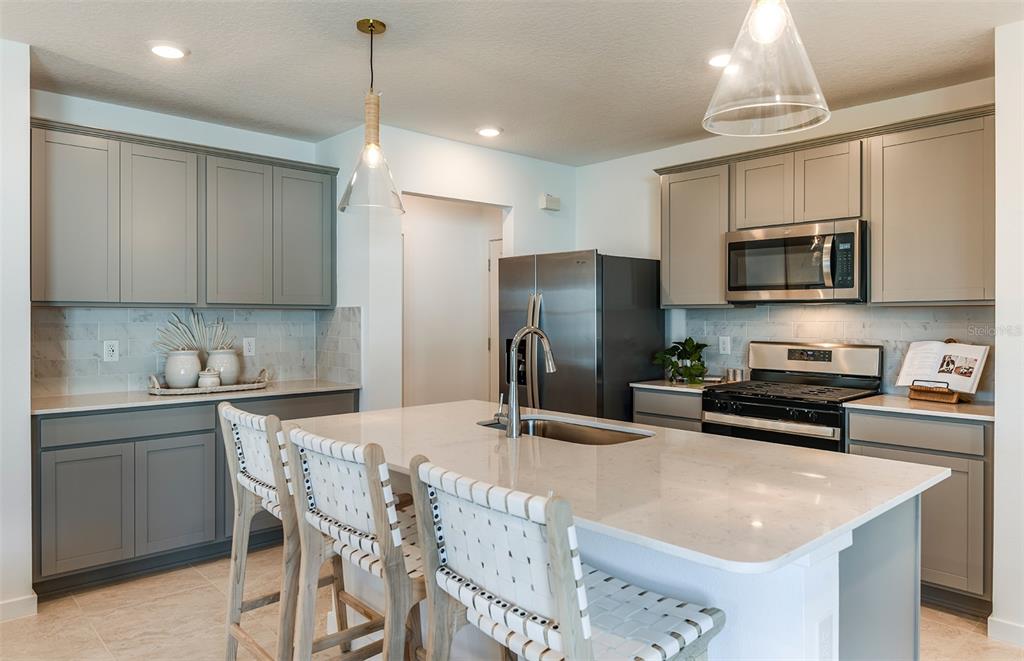 A modern kitchen features gray cabinets, a white quartz island with seating, and stainless appliances — 3705 HORNBEAM ROAD, SPRING HILL, FL