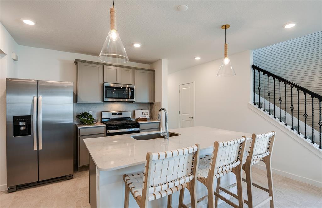 A kitchen features a stainless steel refrigerator, gray cabinets, and a central island with seating — 3705 HORNBEAM ROAD, SPRING HILL, FL