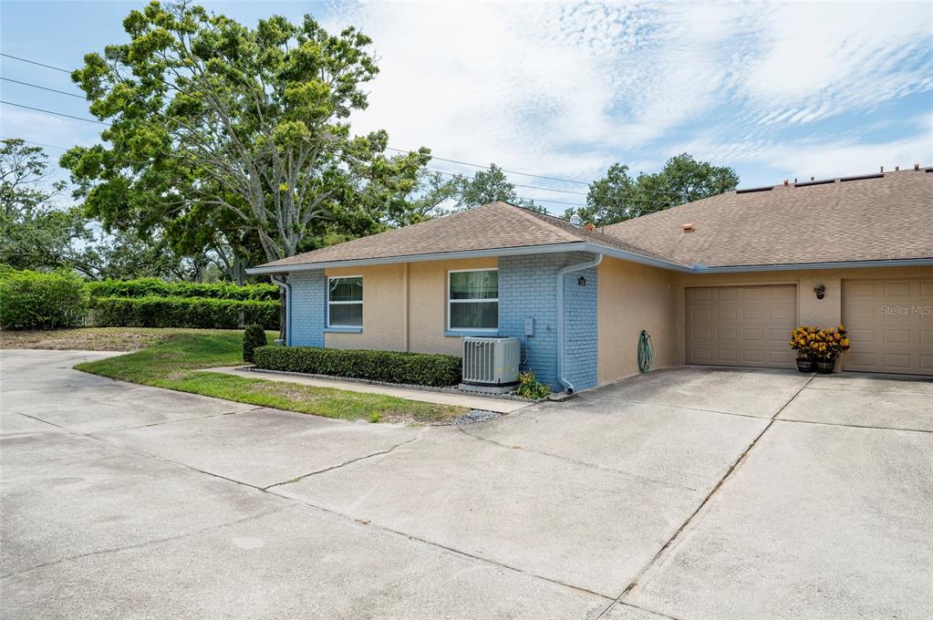A single-story duplex with a tan stucco exterior, blue brick accents, and a concrete driveway — 1245 SUTHERLAND COURT UNIT 1452, DUNEDIN, FL