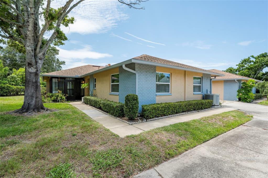 A single-story house with light yellow stucco walls, blue brick accents, and a concrete walkway — 1245 SUTHERLAND COURT UNIT 1452, DUNEDIN, FL