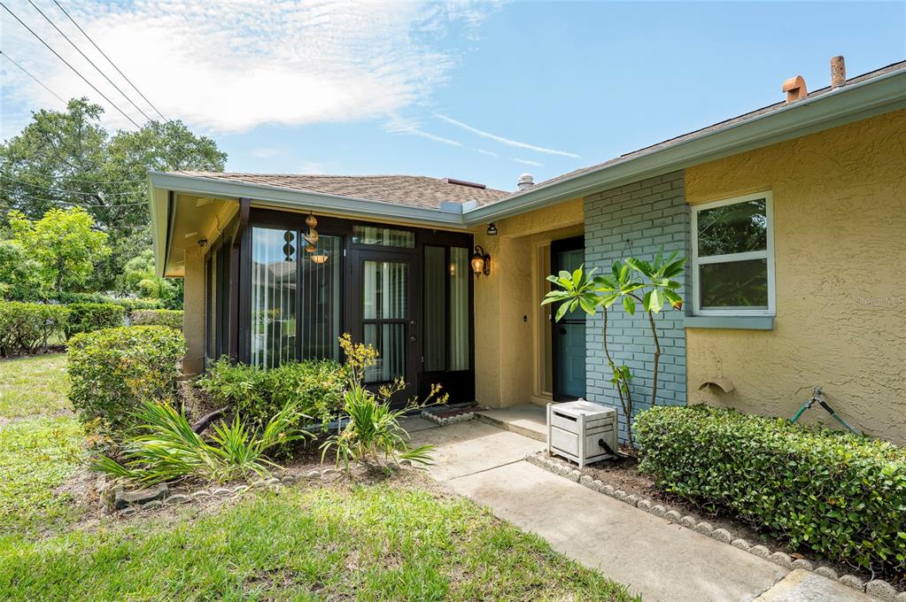 A yellow house exterior features a screened-in porch, a concrete walkway, and a brick accent wall — 1245 SUTHERLAND COURT UNIT 1452, DUNEDIN, FL