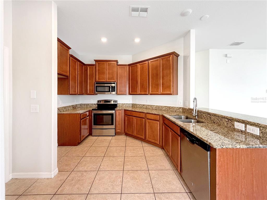 A kitchen features wood cabinets, granite countertops, stainless steel appliances, and beige tile flooring — 1969 HAWKS VIEW DRIVE, RUSKIN, FL
