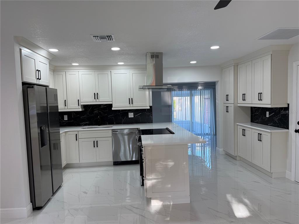 A modern kitchen features white cabinets, stainless steel appliances, a center island, and marble flooring — 1457 MONTEGO LANE, ORLANDO, FL