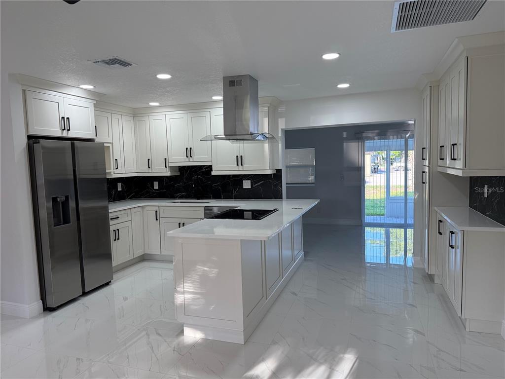 A modern kitchen features white cabinetry, stainless steel appliances, a center island, and marble-look flooring — 1457 MONTEGO LANE, ORLANDO, FL