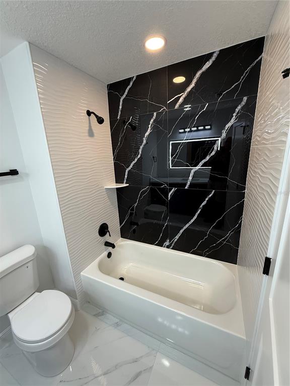 A bathroom features a white tub, black marble-patterned wall tiles, and white wavy side tiles — 1457 MONTEGO LANE, ORLANDO, FL