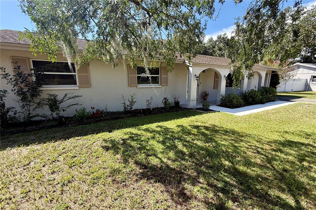 A single-story house with a beige stucco exterior, arched entryway, and brown shingled roof — 12215 ORCHID LANE, THONOTOSASSA, FL