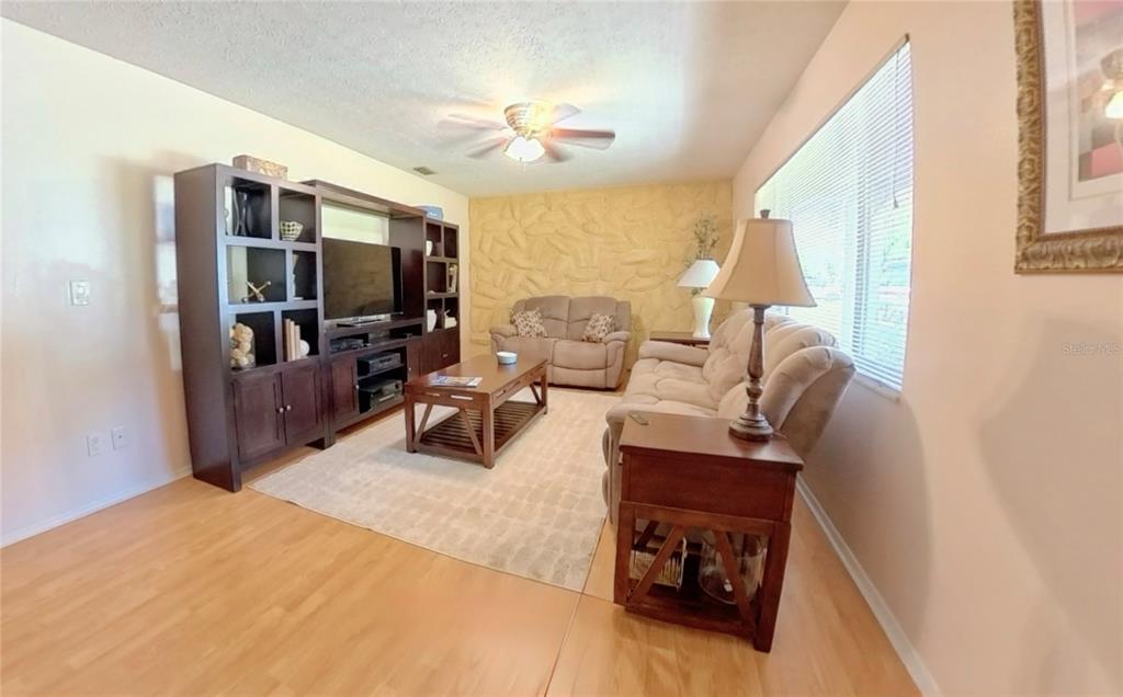 A living room features light wood flooring, a textured accent wall, and a large entertainment center — 12215 ORCHID LANE, THONOTOSASSA, FL