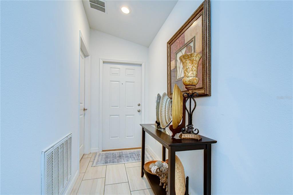 A narrow entryway features tile flooring, a console table with decor, and a white door — 35099 ACKLEY TRACE, ZEPHYRHILLS, FL
