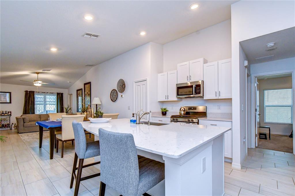 A kitchen with white cabinets and a quartz island overlooks an open-concept dining and living area — 35099 ACKLEY TRACE, ZEPHYRHILLS, FL
