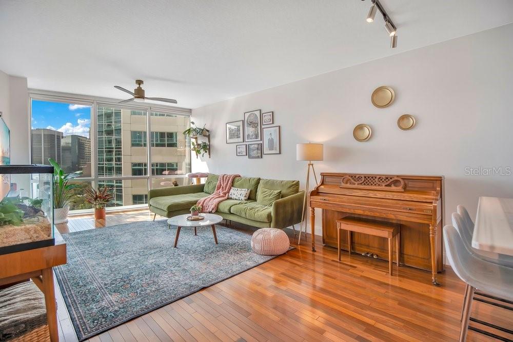 A living room features a green sectional sofa, a piano, and floor-to-ceiling windows — 322 E CENTRAL BOULEVARD UNIT 1005, ORLANDO, FL