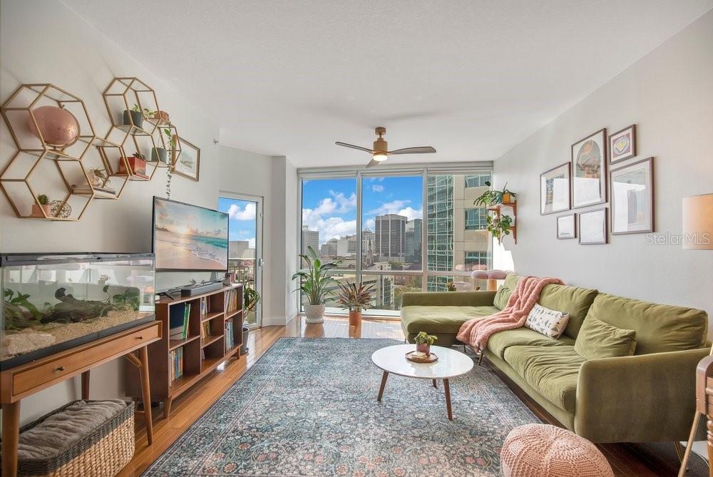 A living room features a green sectional sofa, a patterned rug, and floor-to-ceiling city windows — 322 E CENTRAL BOULEVARD UNIT 1005, ORLANDO, FL